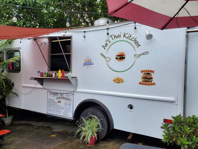 The white Ae’s Thai Kitchen burger truck with a burger on its logo and a Chicken Sandwich decal