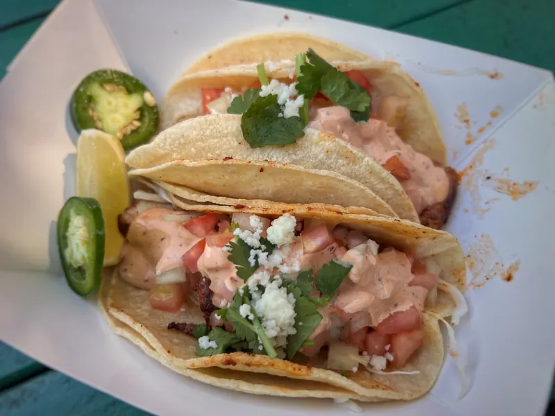 Fish tacos on corn tortillas with chipotle sauce, queso fresco, cilantro, jalapeño and lime