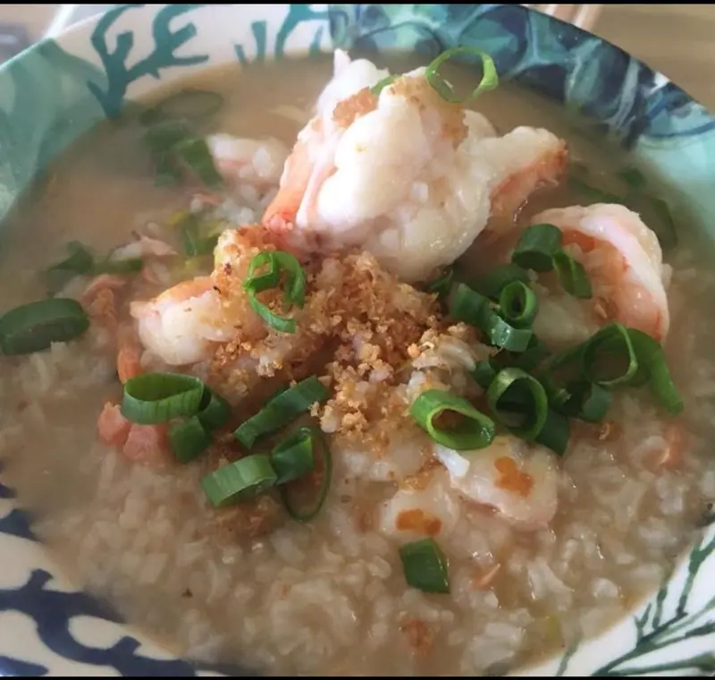Rice soup with shrimp, fried garlic and green onion in a blue and white bowl