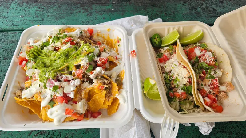 Nachos with guacamole next to an order of fish tacos with lime