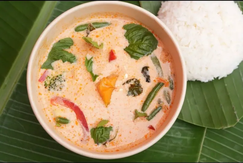 Pumpkin red curry with Thai basil, green beans and red pepper, with a scoop of rice on banana leaves