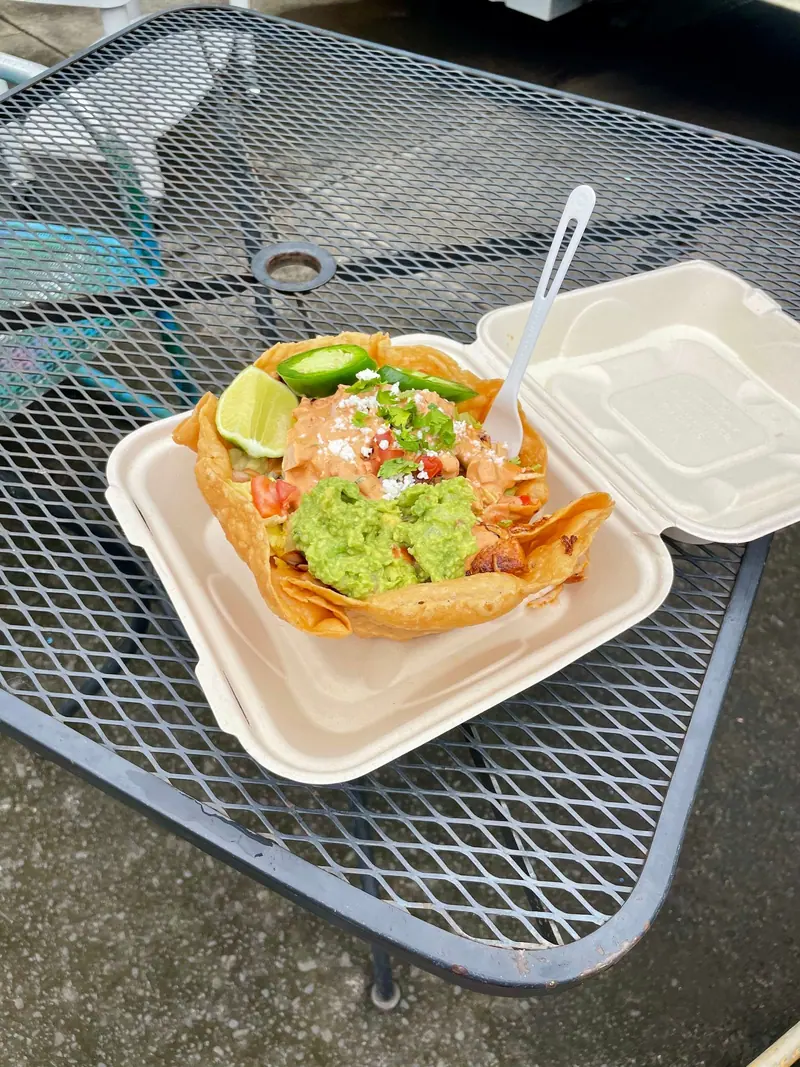 A taco salad bowl with guacamole, jalapeño and lime on a picnic table