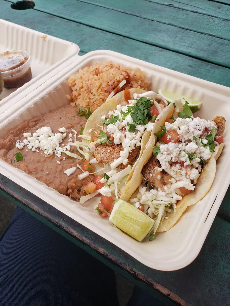 A taco plate with two fish tacos, rice and refried beans with queso fresco