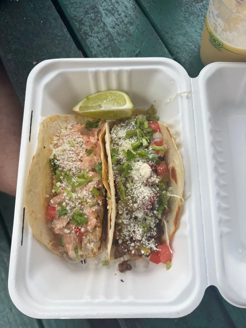 Fish and carne asada tacos on corn tortillas with lime in a takeout box